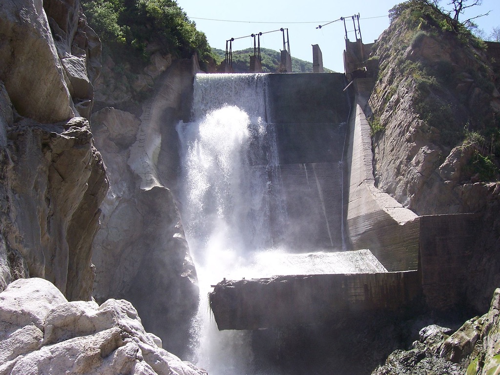 Water cascades over the edge of a tall dam and pours between large walls of rock.